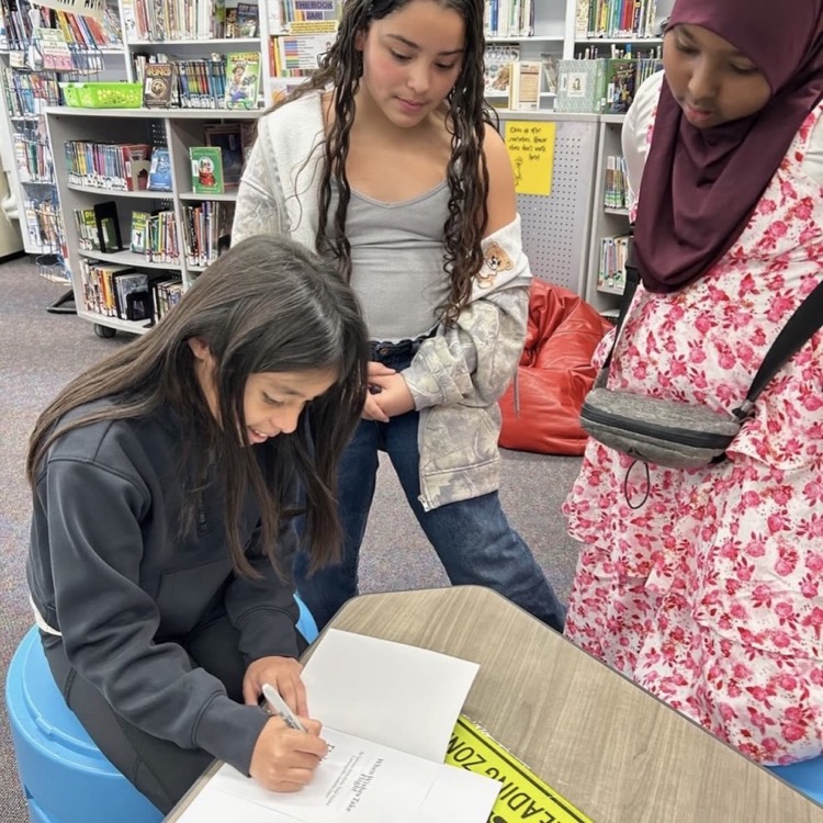A student signing her printed book while two other students look on in the school library